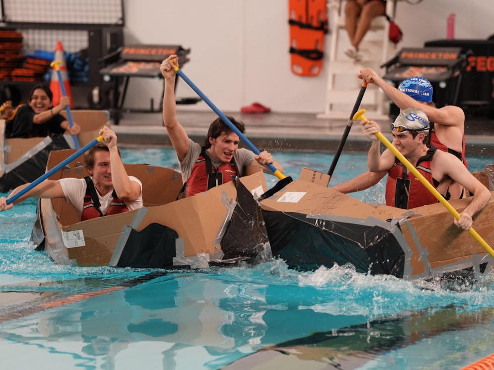 Four men paddling across a swimming pool in homemade cardboard boats.