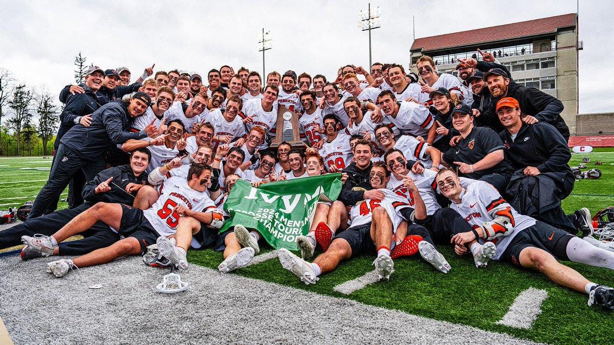 Men’s team in white and orange uniforms celebrate victory with trophy on field.
