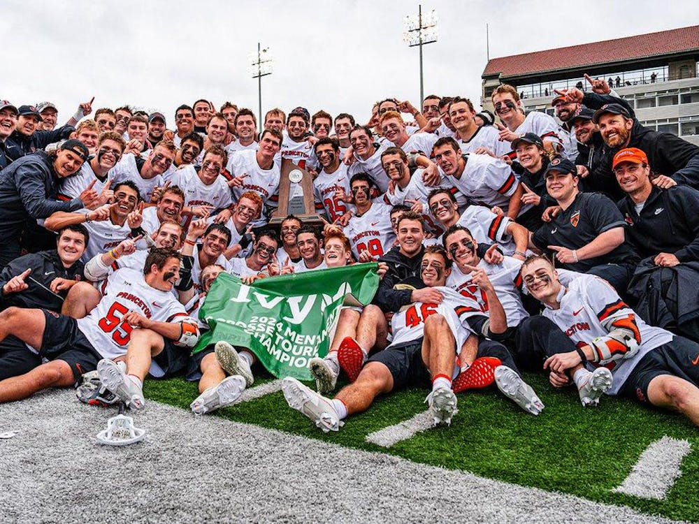Men’s team in white and orange uniforms celebrate victory with trophy on field.