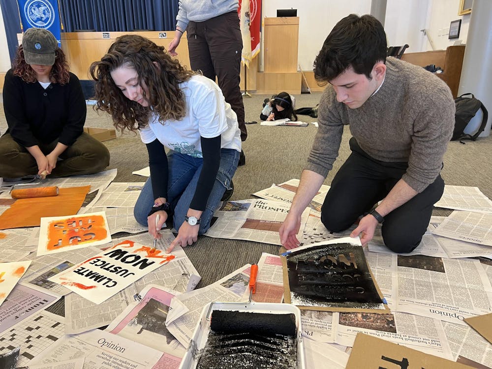 Two students kneel on the floor and paint posters for climate action protests.