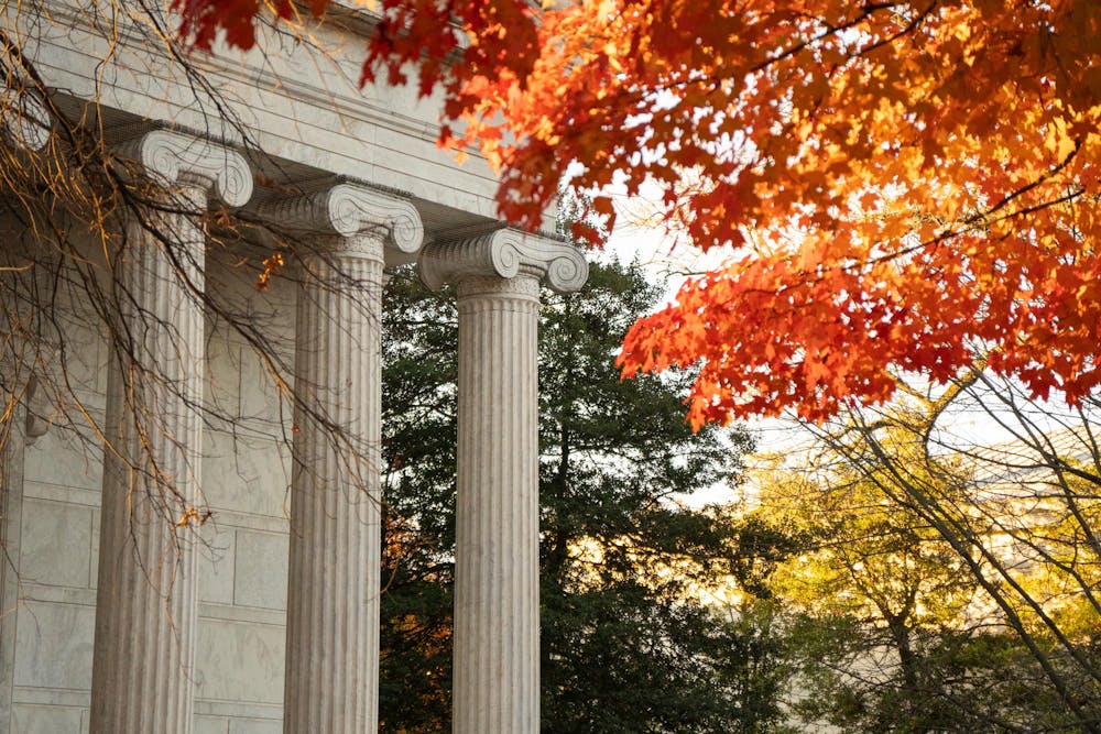 Building with white marble columns in front of a red fall tree. 