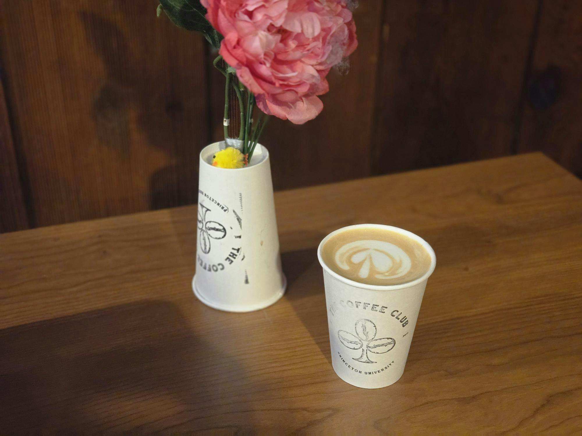 A white Coffee Club cup and a white upside down Coffee Club cup sit on a brown desk.
