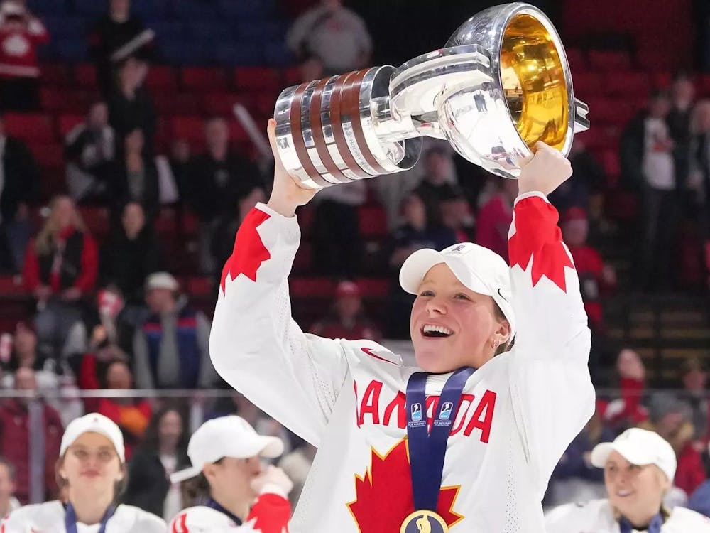 A woman with a medal around her neck holds up a trophy in the air on an ice hockey rink. 