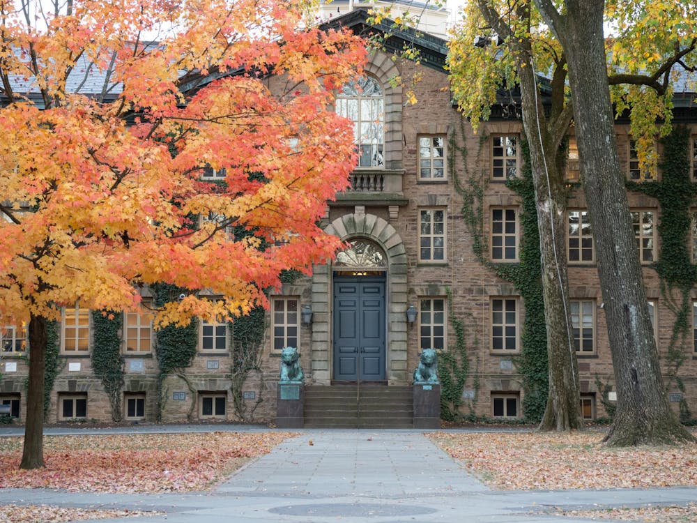 Brown stone building with many windows, ivy growing on it, and a tree with orange leaves in front.