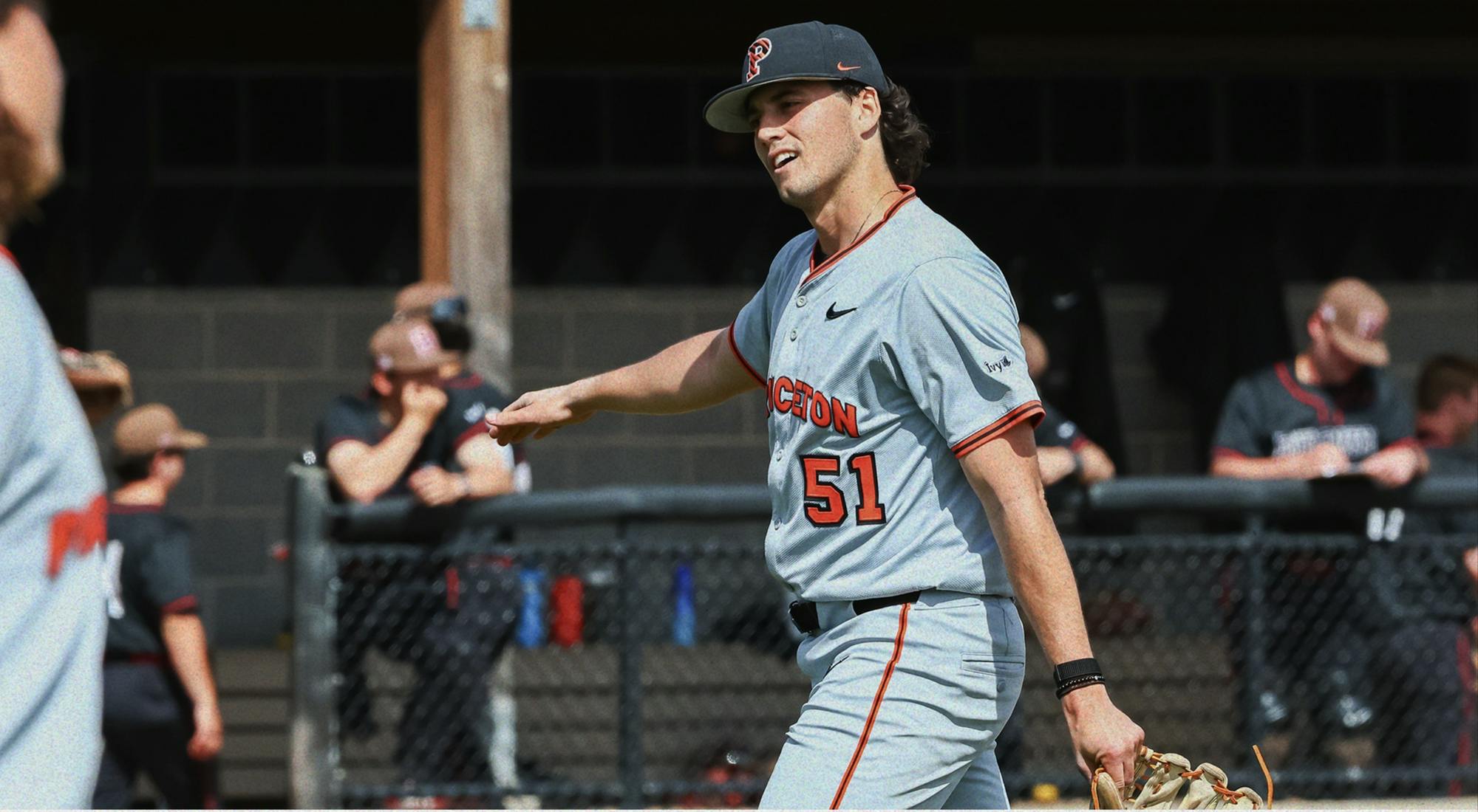 A baseball player in a gray uniform struts off the field with his glove in his left hand.