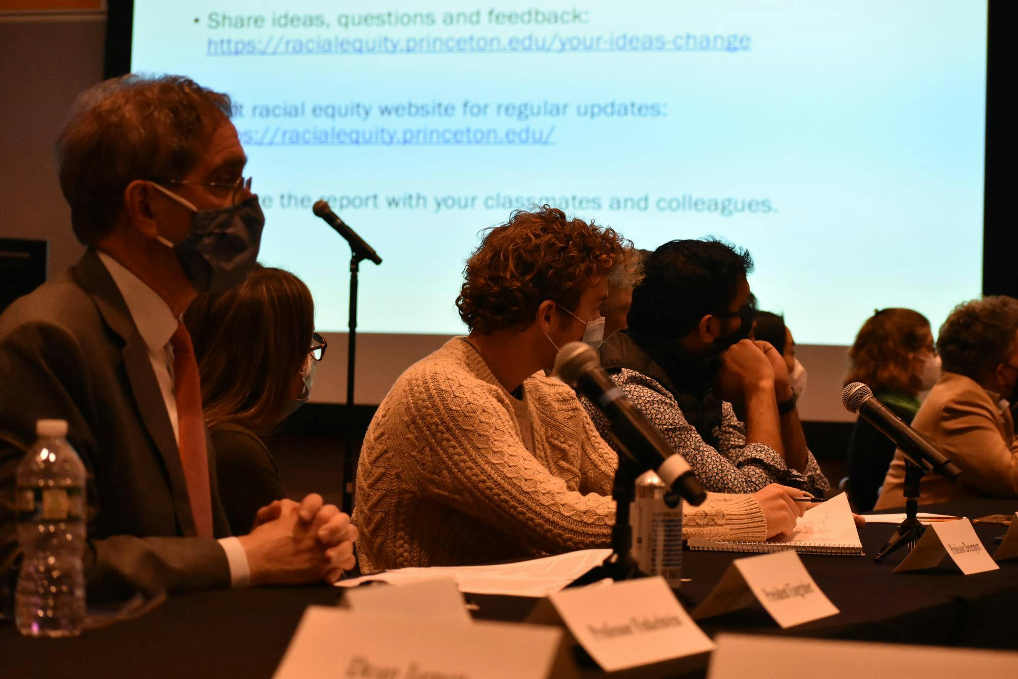 Landscape photo of a few people sitting in front of a table with microphones.