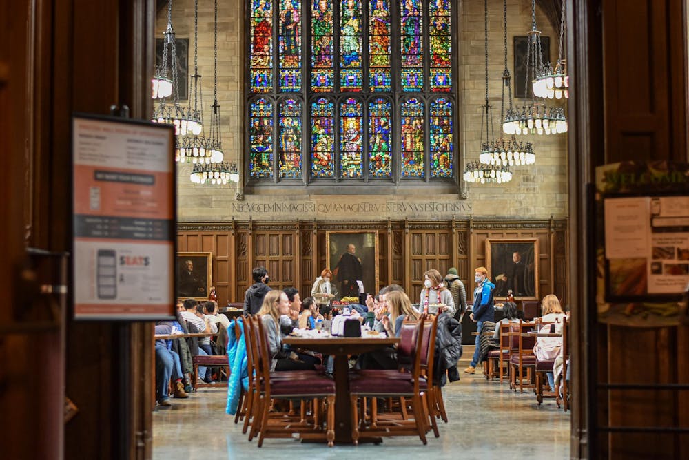 People sit at a long table in front of wood paneling and a large stained glass window