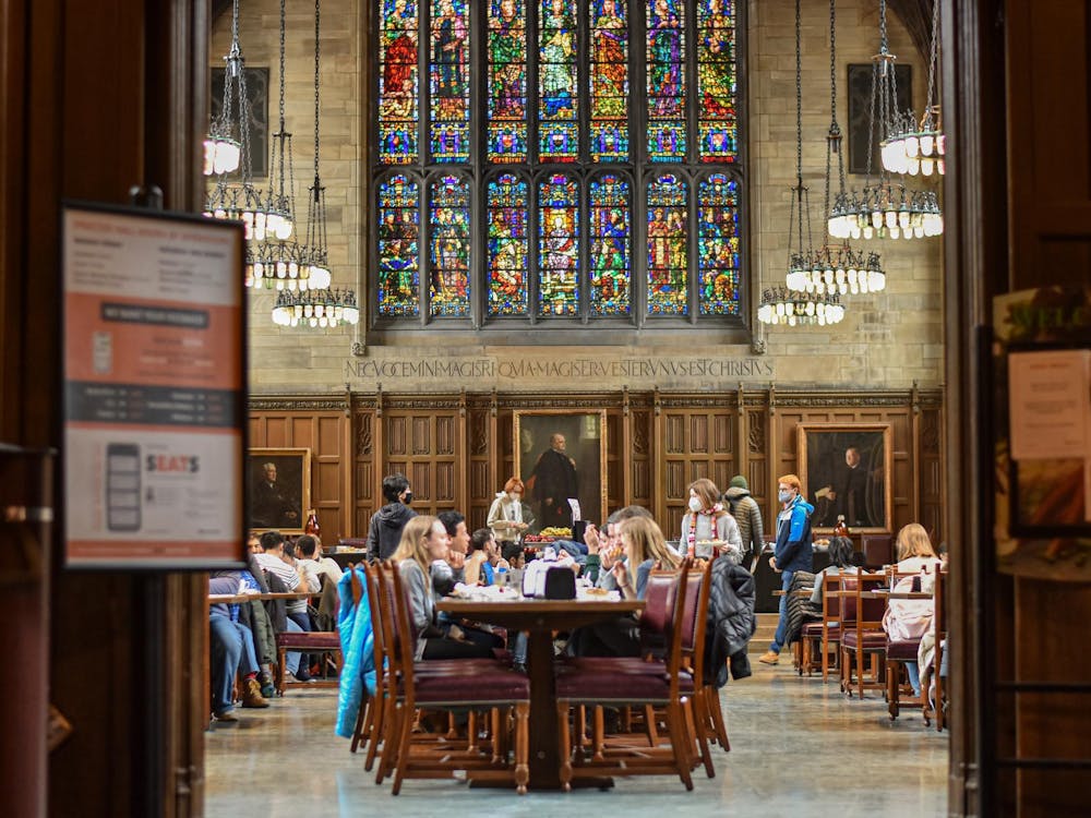 People sit at a long table in front of wood paneling and a large stained glass window