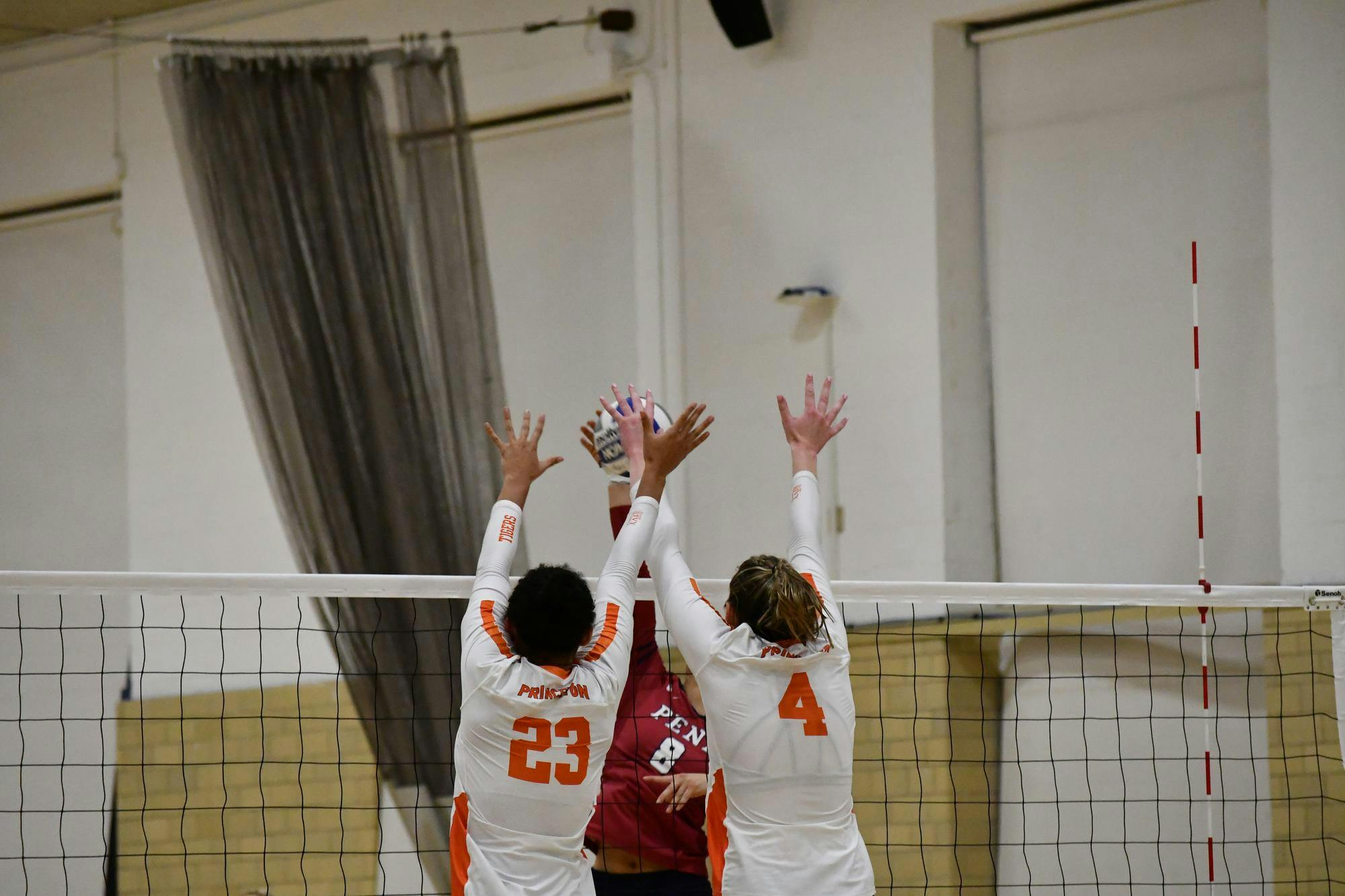 Two Princeton volleyball players jump above the net to block a hit by an opposing team player. 