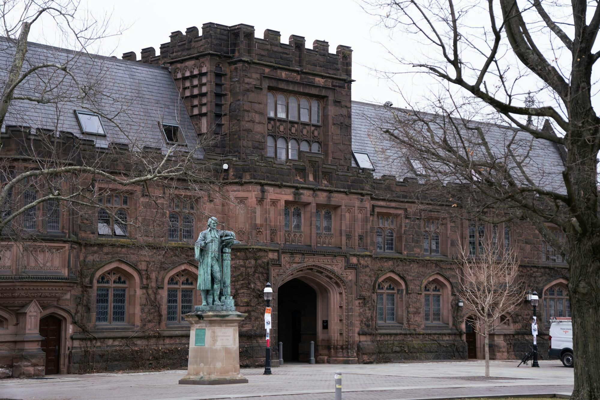 A grey sky over a brick building. A greening statue stands in front of it. 