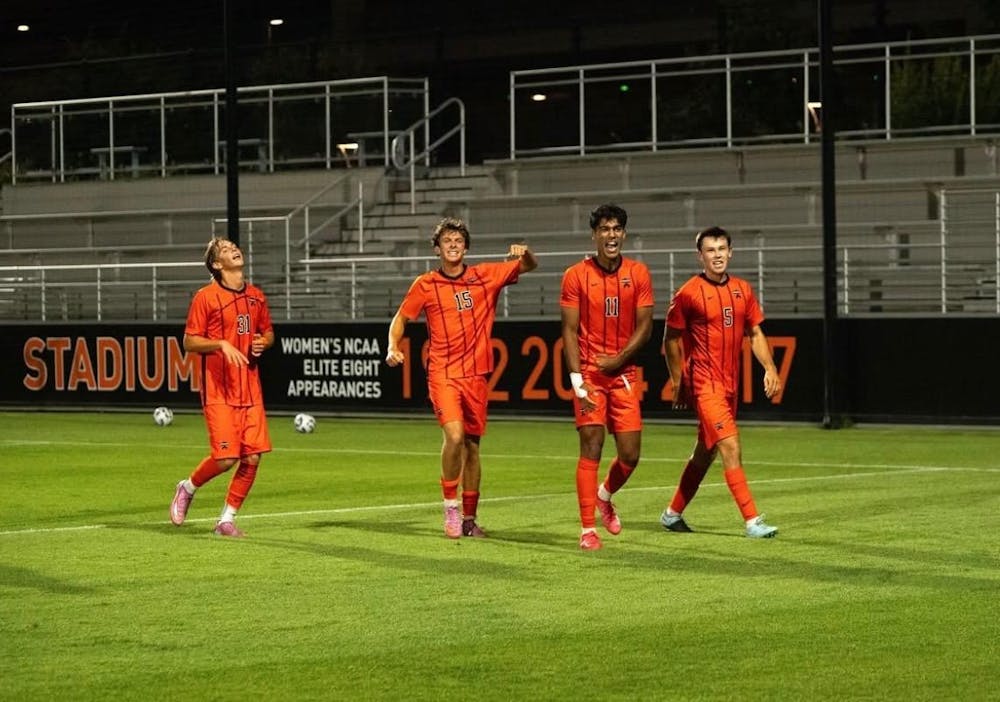 four soccer players in orange jerseys celebrate on a soccer pitch at night