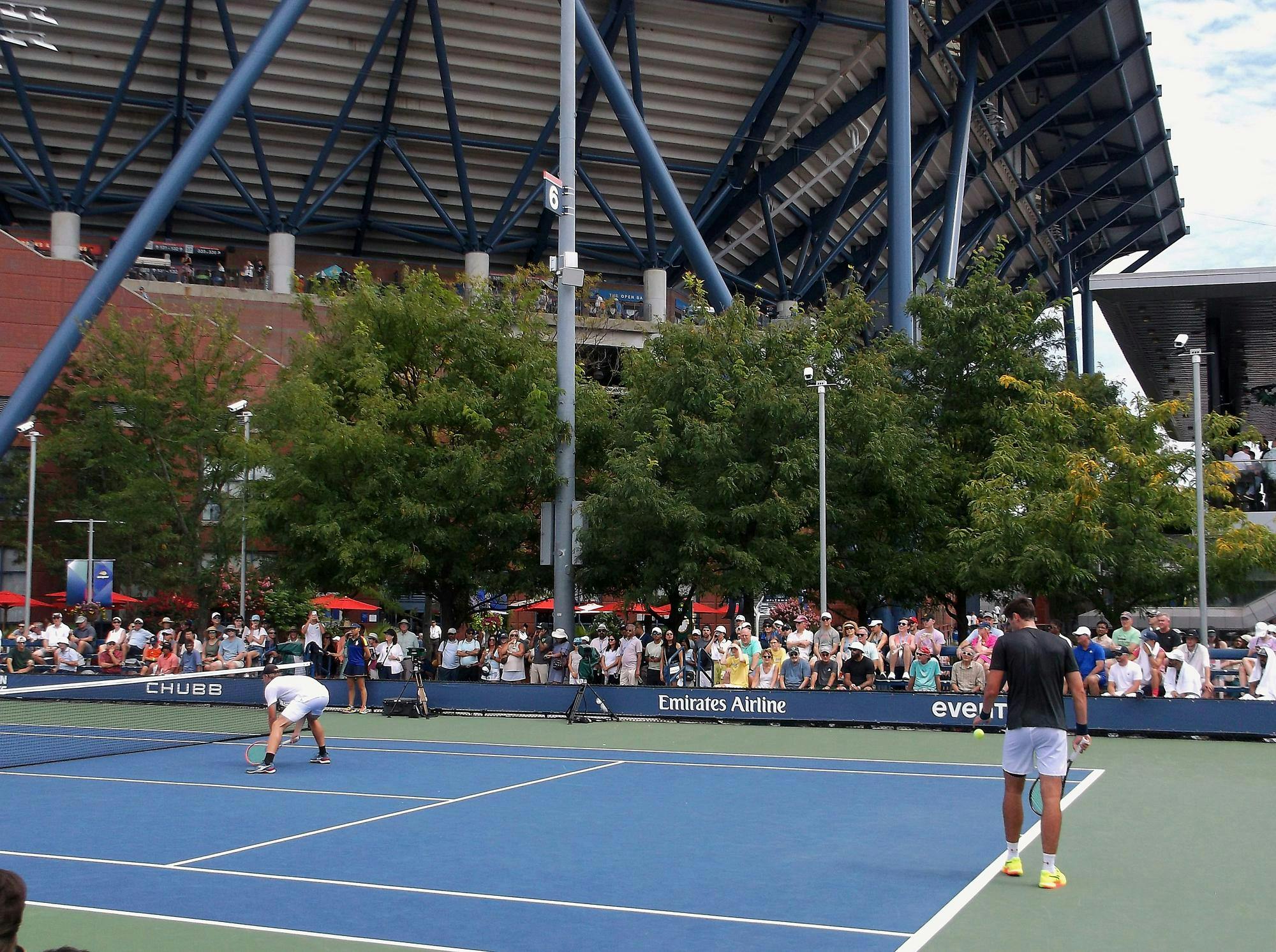 Man in grey shirt prepares to serve tennis ball