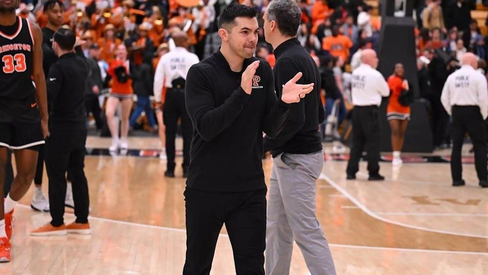 Princeton coach claps on the court as players, staff, and fans are visible in the background.