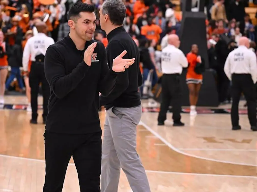 Princeton coach claps on the court as players, staff, and fans are visible in the background.