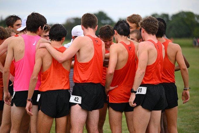 group of guys in orange and black uniforms huddle before starting the run 