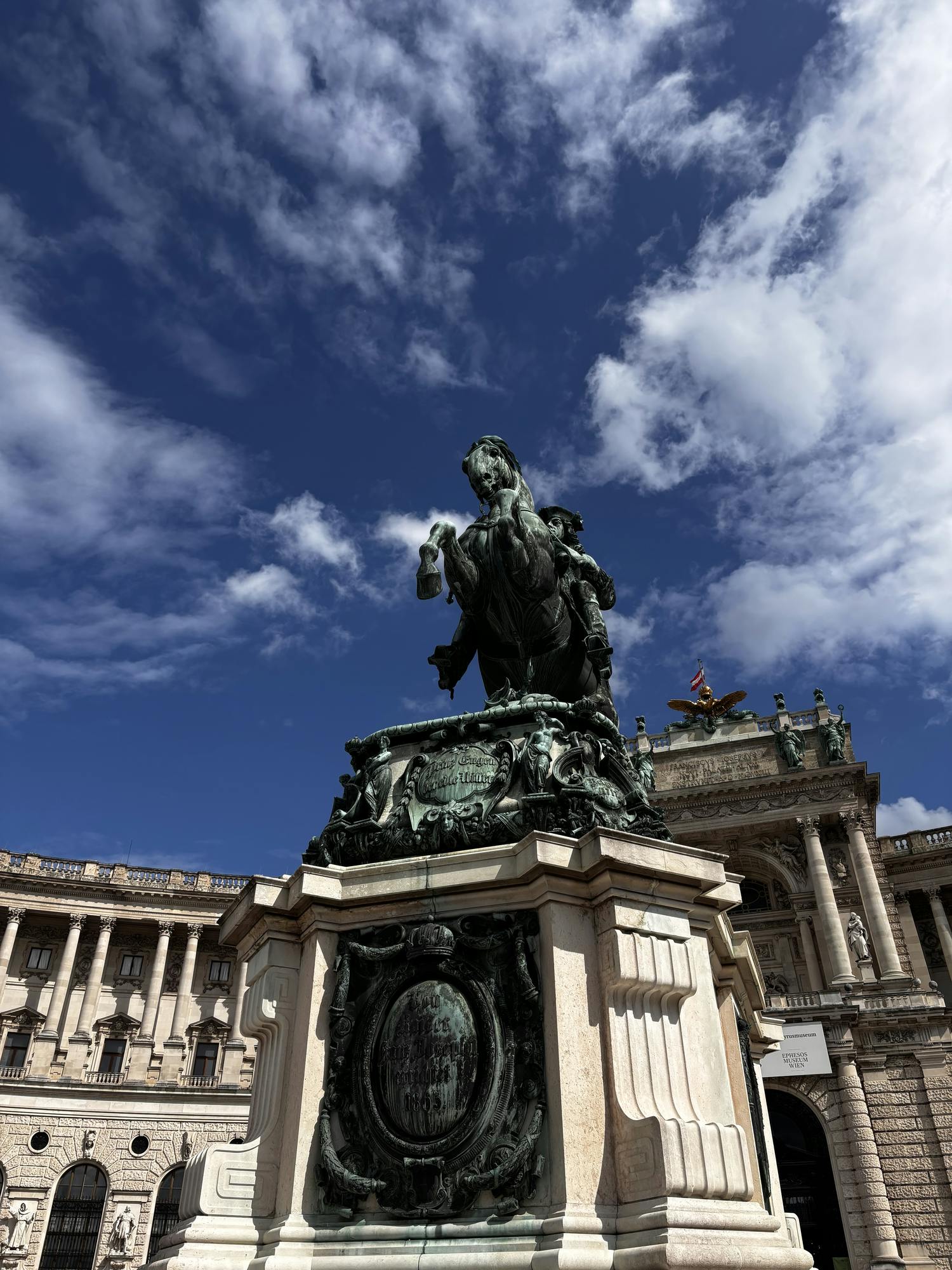 A statue of a horse with a rider in front of an adorned building with pillars. 