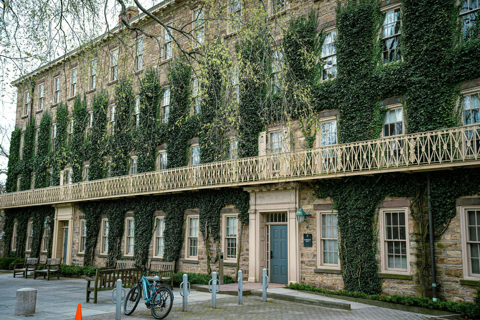 A large, ivy-covered building looms in front of the camera. Benches and bike racks are outside. 