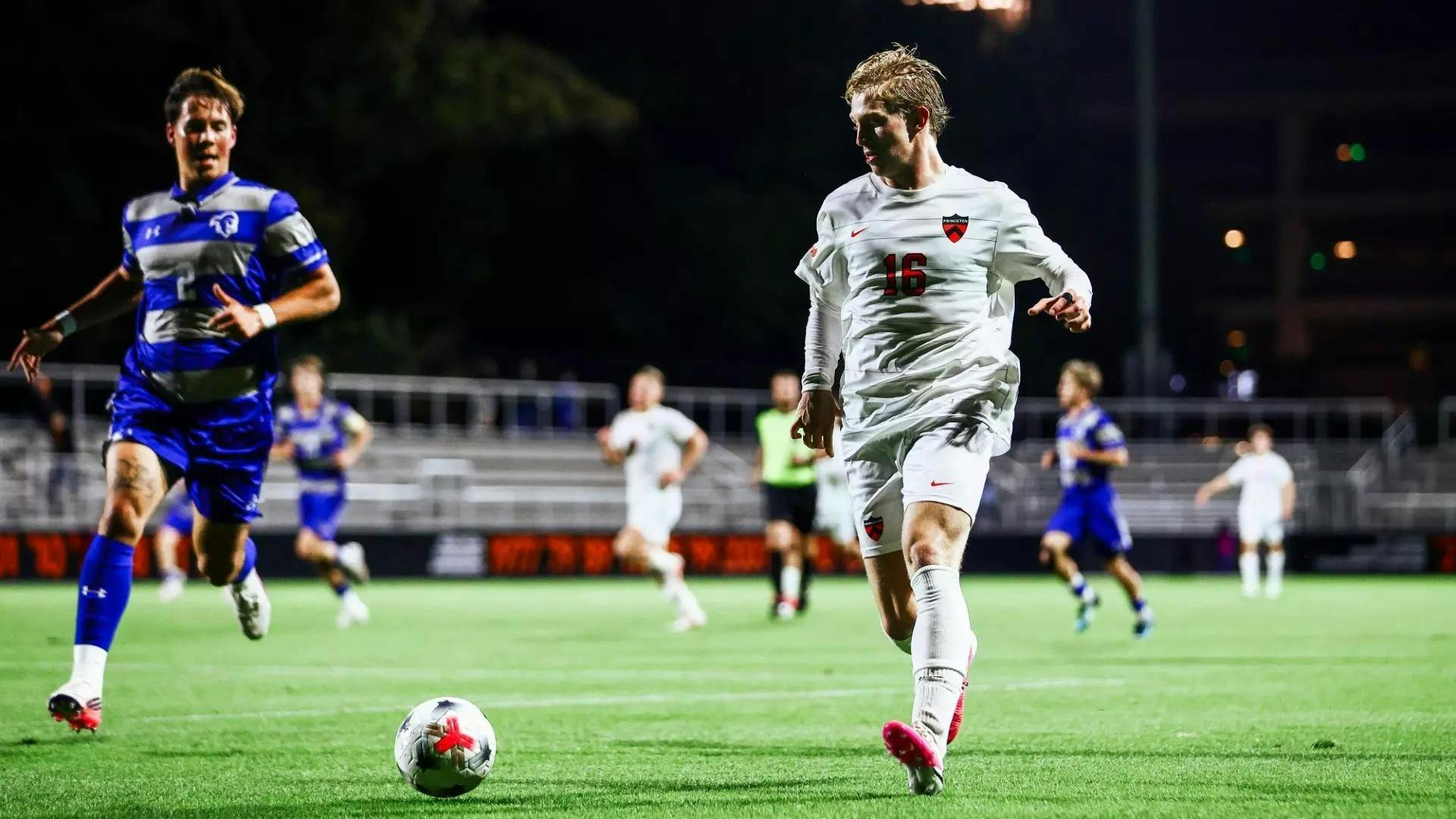 A man in a white and orange jersey dribbles the ball past a defender.