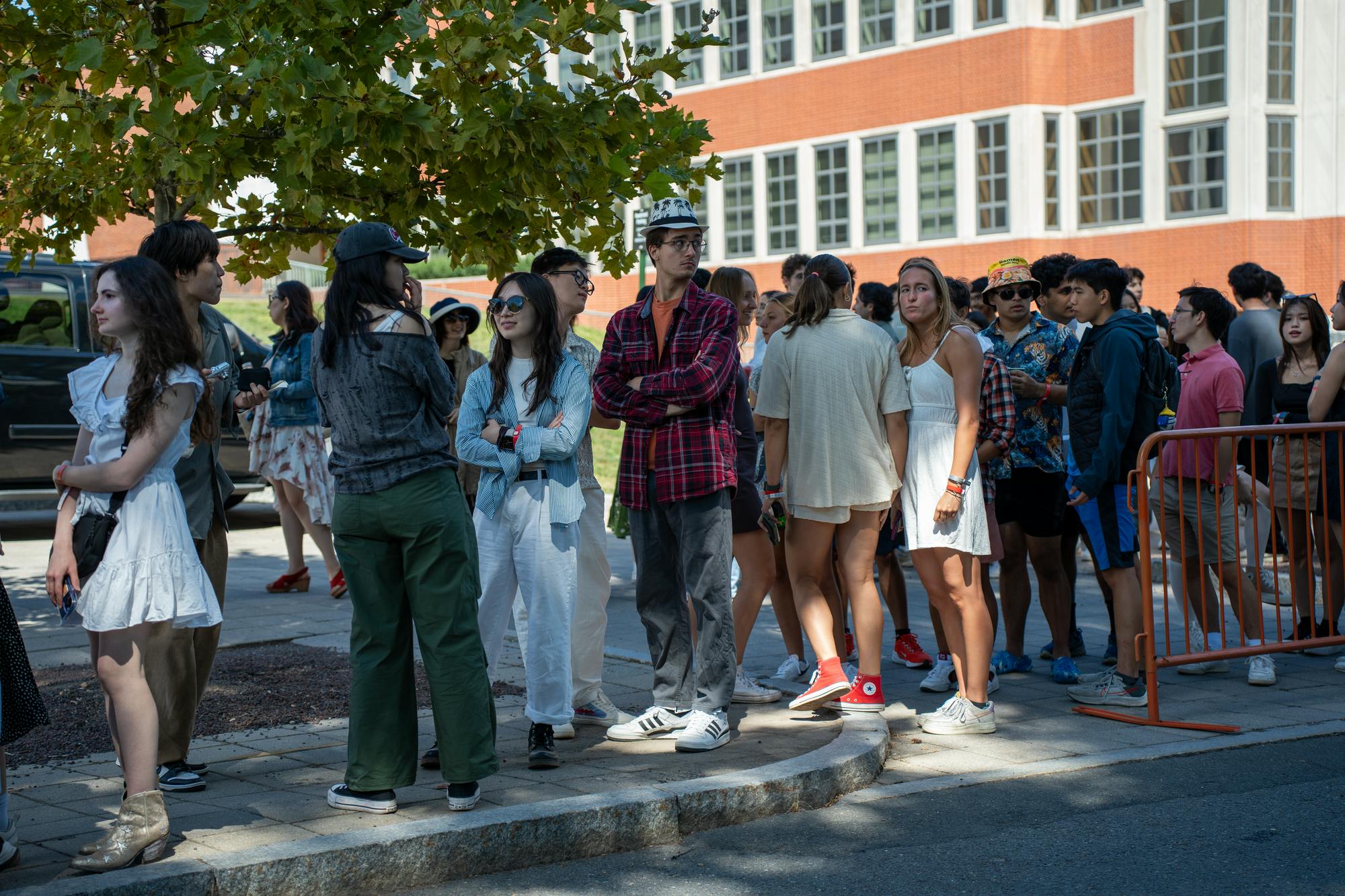 Students stand in a long line on a sidewalk.