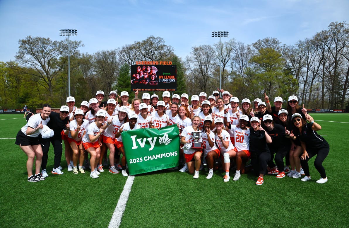 Princeton women's lacrosse posing in front of Ivy League championship banner.