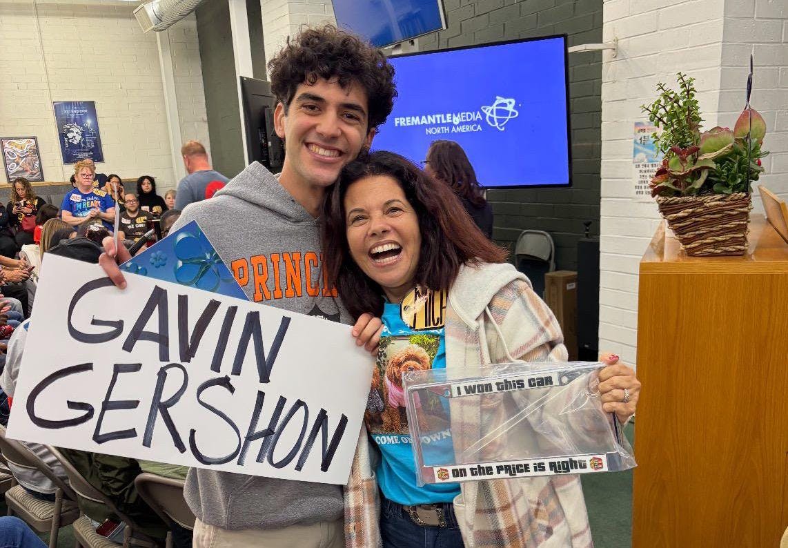 A young man with dark hair holds a sign that reads “Gavin Gershon” and a woman with brown hair is holding a license plate.