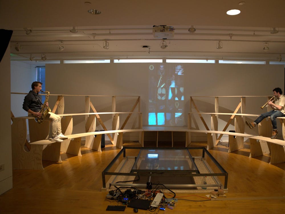 The setup of the exhibition, with wooden benches surrounding the scanner in the center. There are scans projected onto a wall behind the benches. 