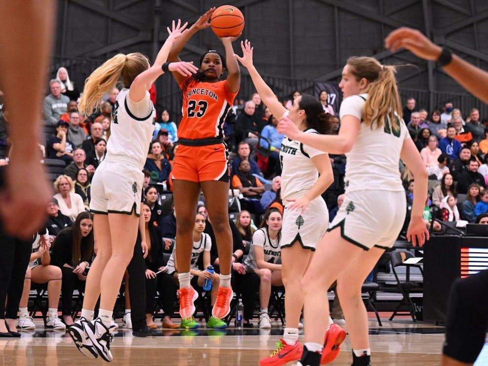 Player in orange and black Princeton jersey shoots a three pointer over two Dartmouth defenders. 
