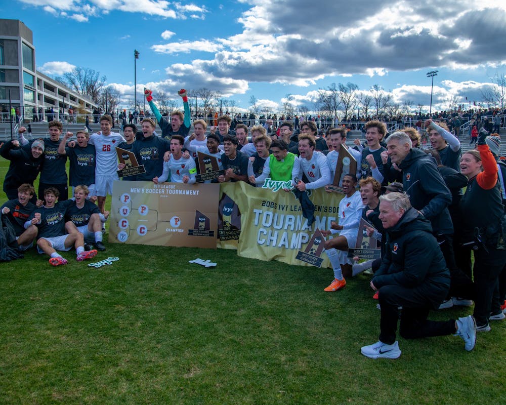 Princeton men’s soccer players and coaches celebrate on the field with trophies and a championship banner after winning the Ivy League tournament.