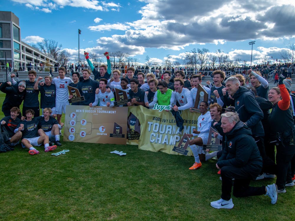Princeton men’s soccer players and coaches celebrate on the field with trophies and a championship banner after winning the Ivy League tournament.