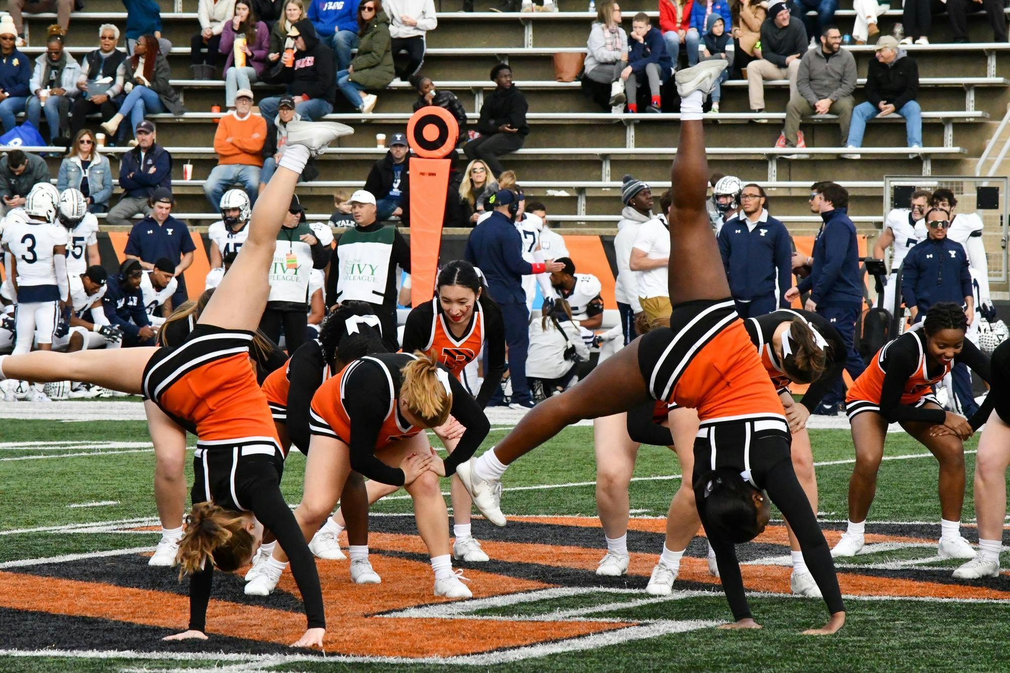 2 Princeton cheerleaders do cartwheels with multiple other cheerleaders dancing in the background.