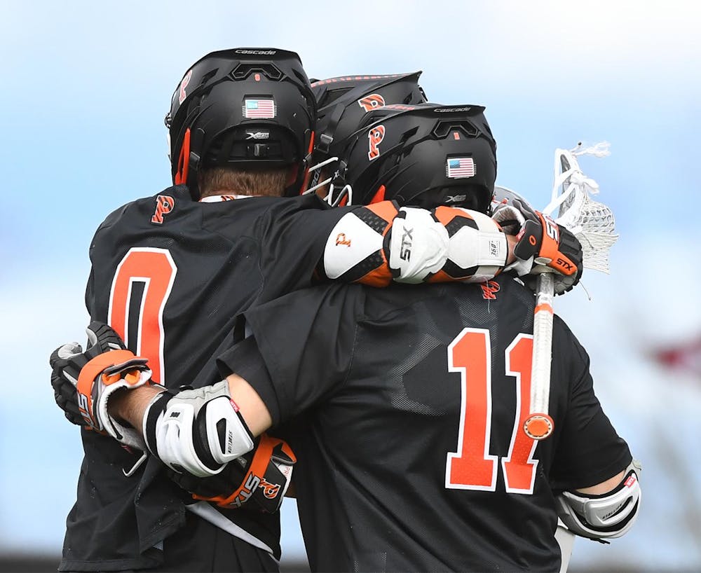 Three lacrosse players in black jerseys and helmets huddle up.
