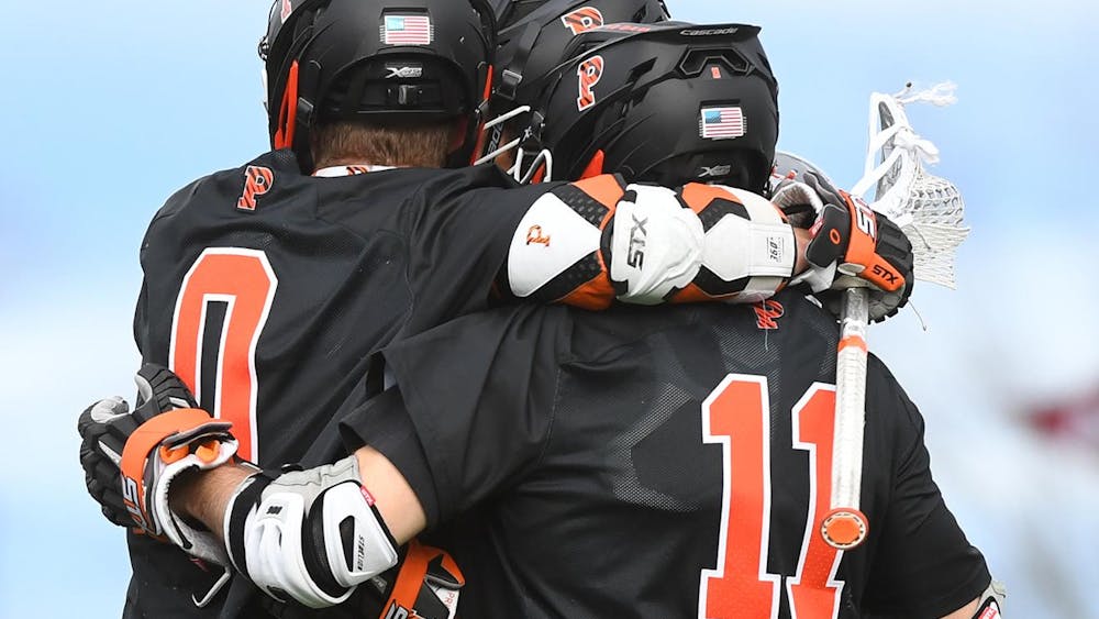 Three lacrosse players in black jerseys and helmets huddle up.