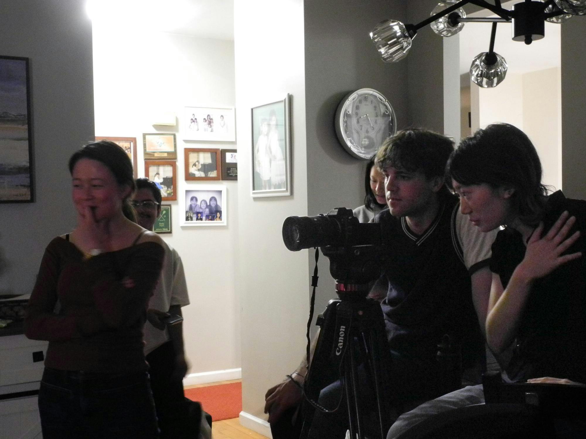 Three people in multicolored outfits are behind a black camera.