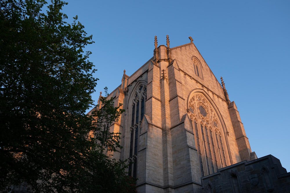 A tall gothic chapel with one face cast in warm colors from the morning sun. 