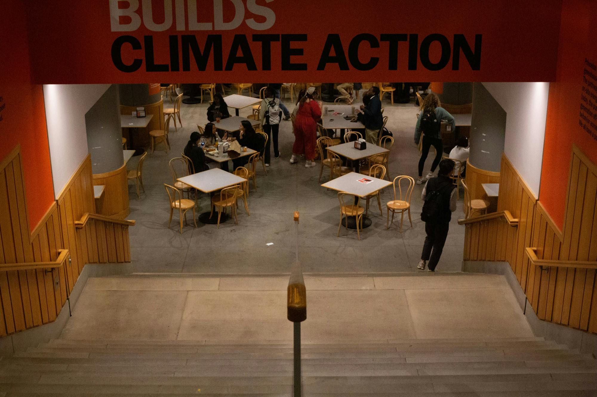 Concrete staircase leading into dining area with people seated at square wooden tables. Banner above the stairway reads "Builds climate action" 