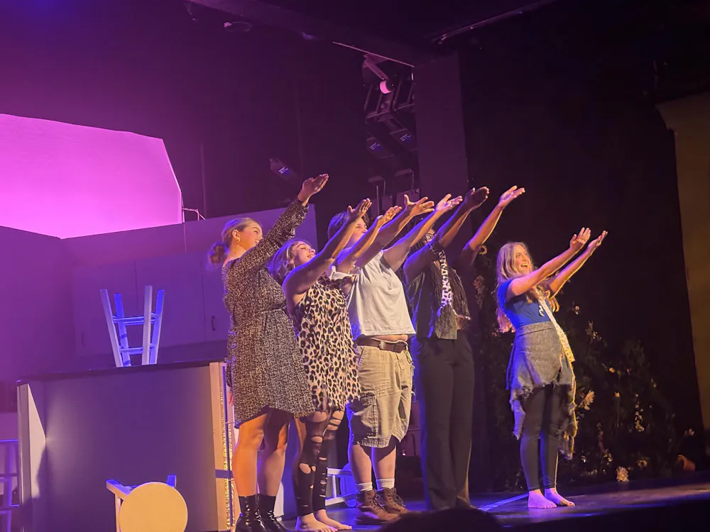 Five actors gesture out beyond the stage to the audience.