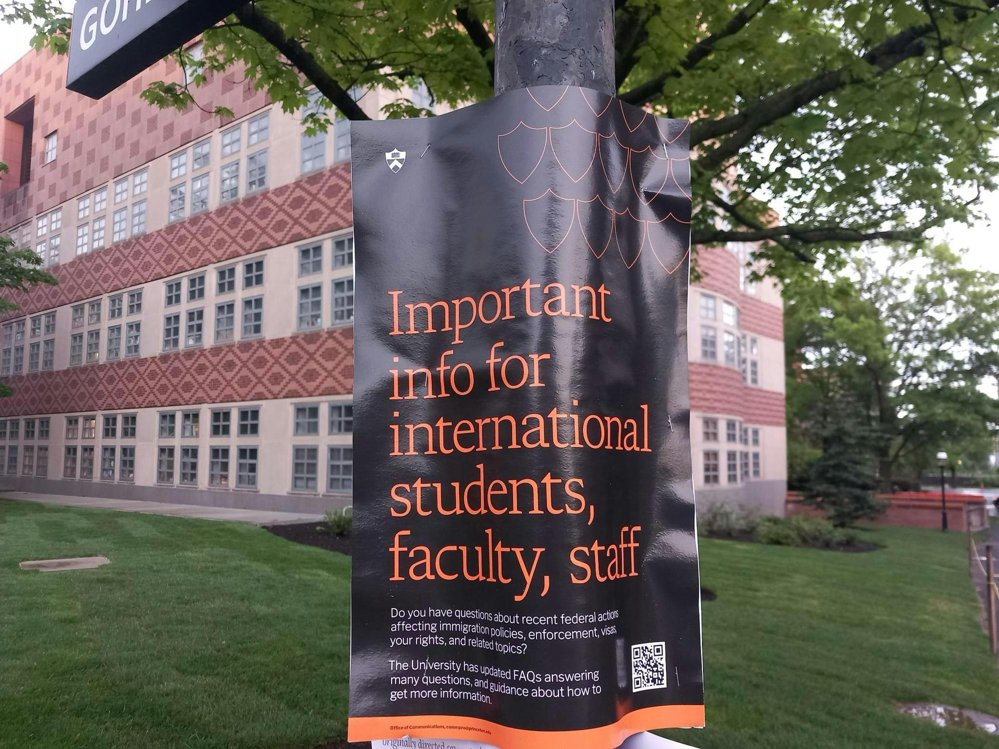 Poster on a pole in front of a building with a green lawn.