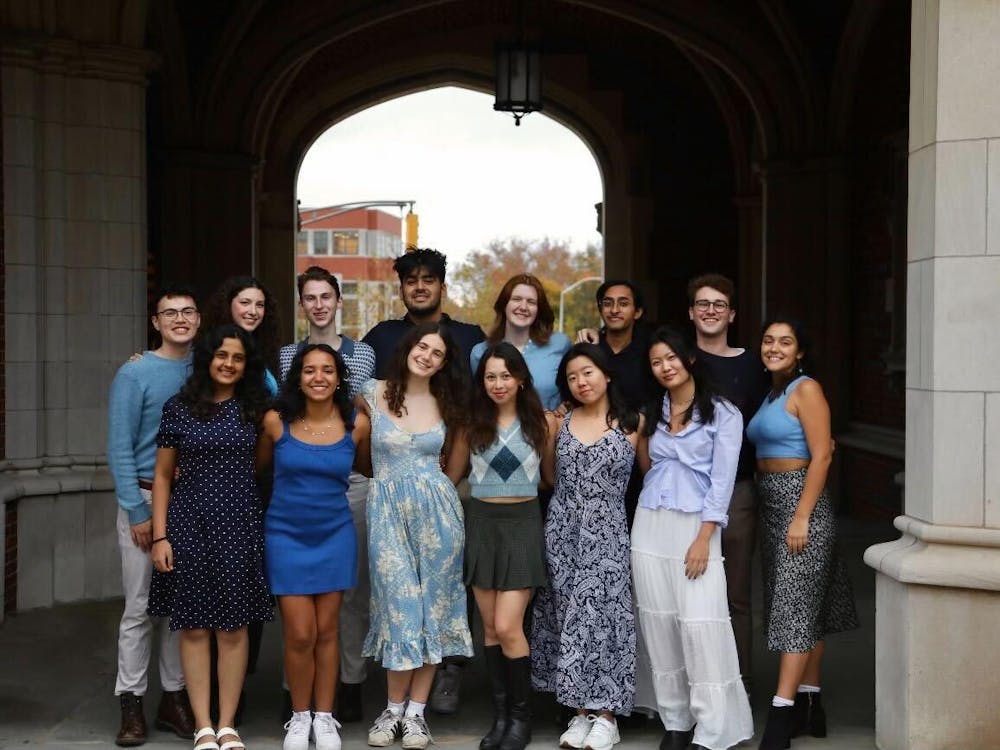 Group photo of 14 students dressed in blue, standing under an arch.