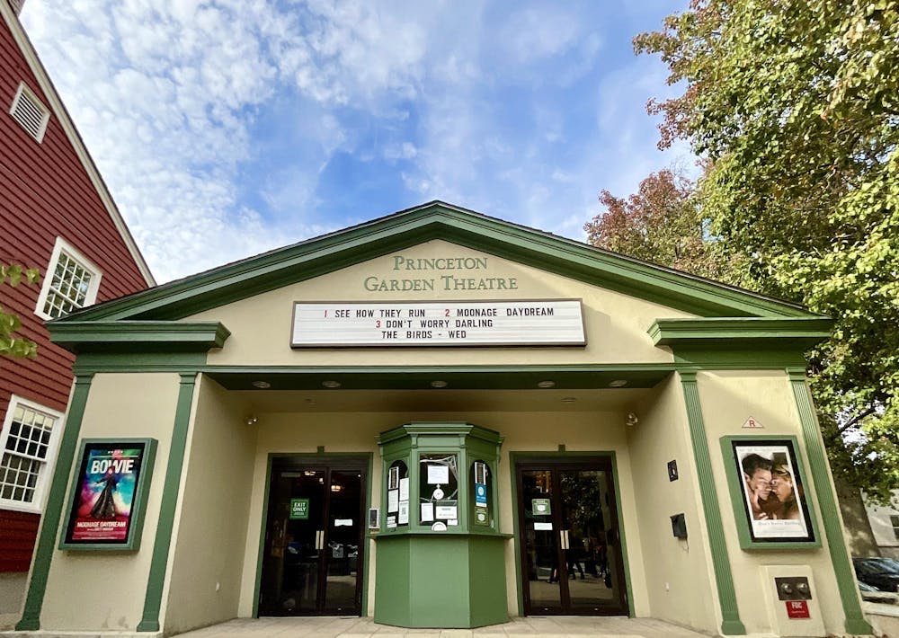 A tan and green movie theater stands with various colorful movie posters under a clear blue sky.  