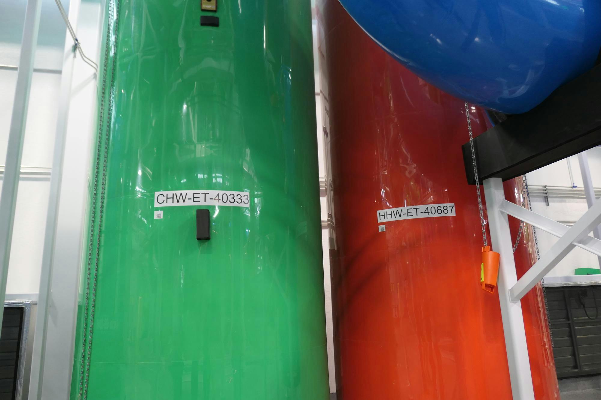 A green chilled water pipe (left) and orange hot water pipe (right), labeled with the plant’s code for identifying equipment. 