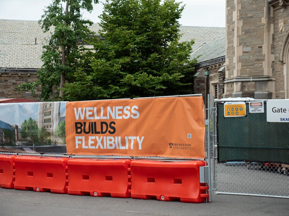 Orange barricades attached to a fence with an orange banner which reads “Wellness builds flexibility”
