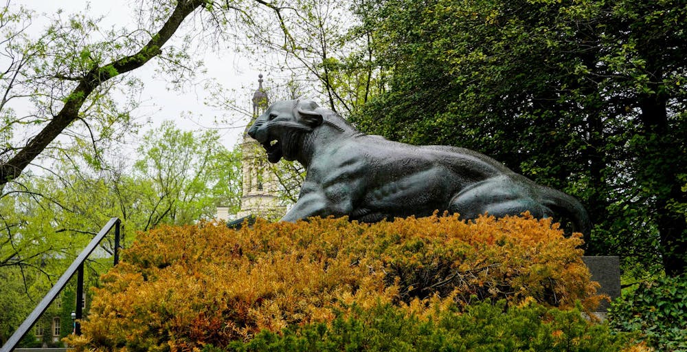 Gray roaring tiger statue alongside fall shrubbery.