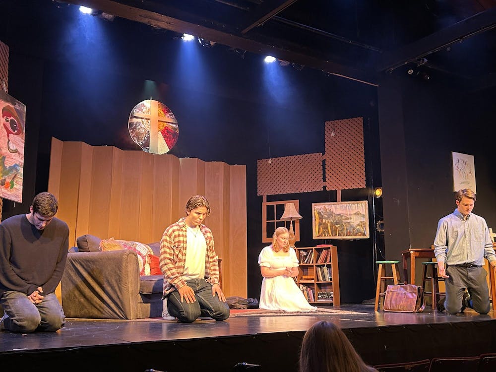 Four individuals are kneeled down and praying on stage as part of the opening scene of the play. 