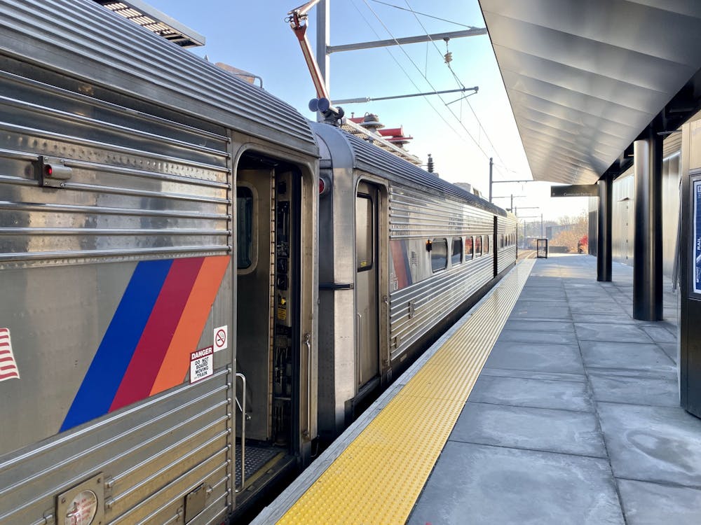 A silver, steel train has a blue, maroon, and orange stripe on it.