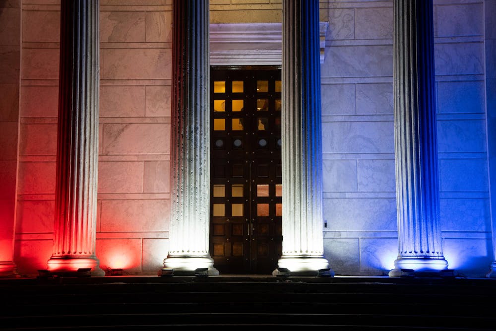 A white marble building with white columns in front, lit up with red and blue lights