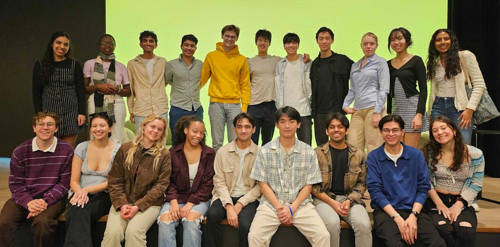 A group of students smile in a group photo in front of a green backdrop.