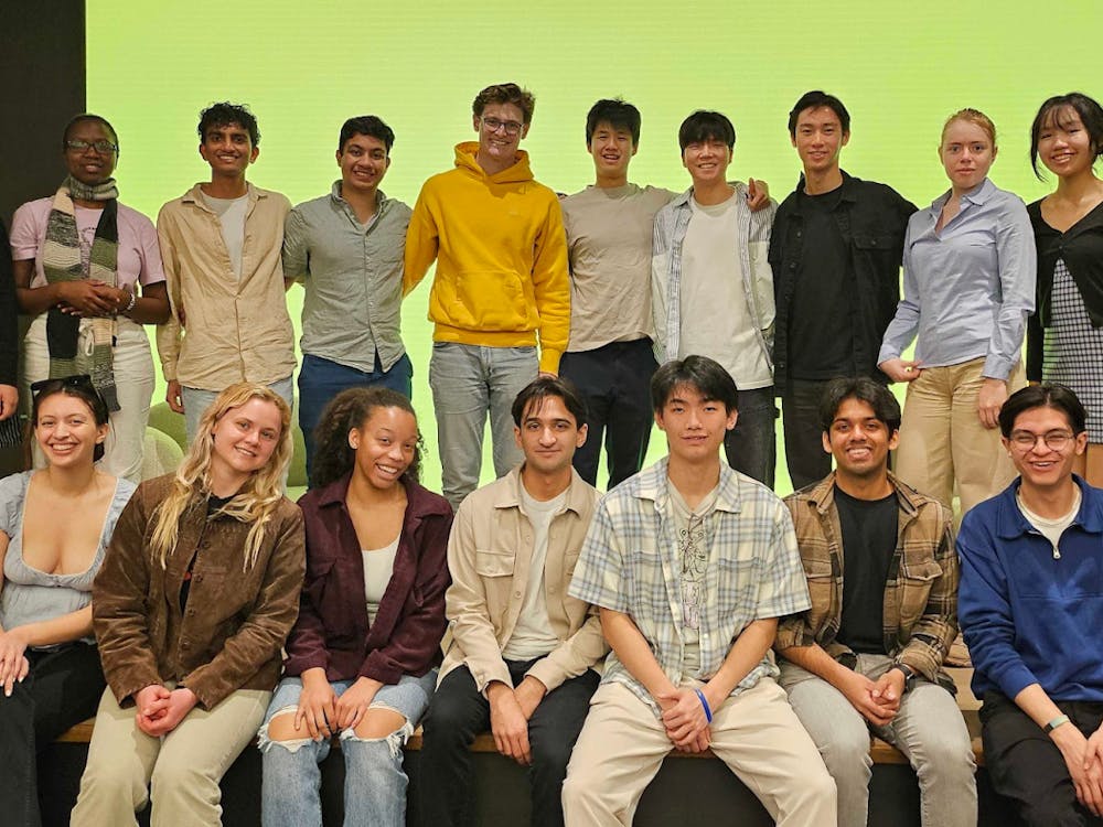 A group of students smile in a group photo in front of a green backdrop.