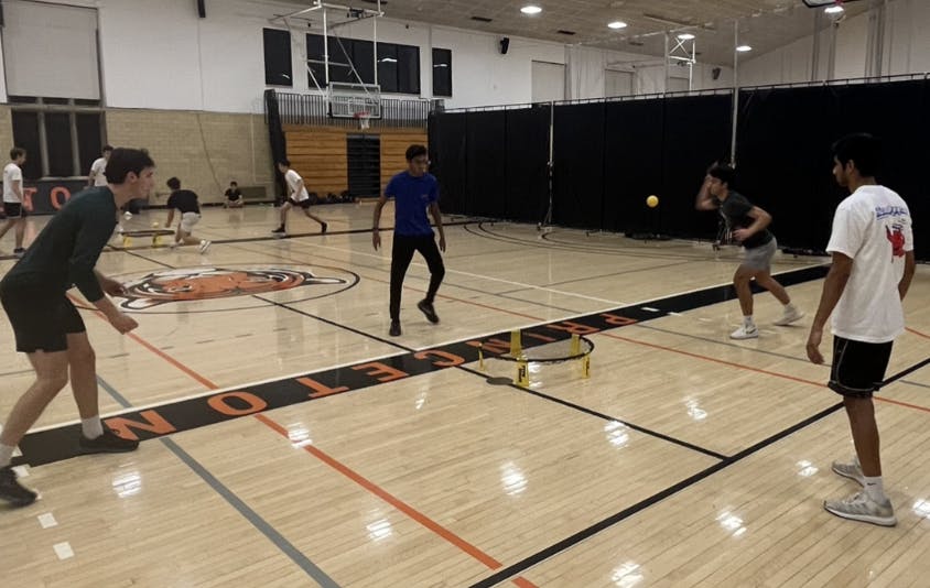 Four men on a court slapping a ball on a circular net 
