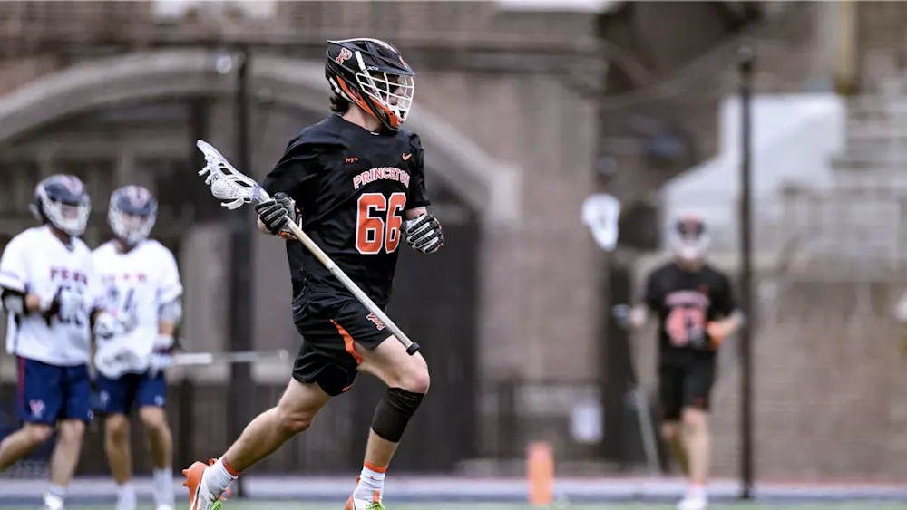 Men's lacrosse player in black uniform and orange writing holding stick behind him looking for a pass.