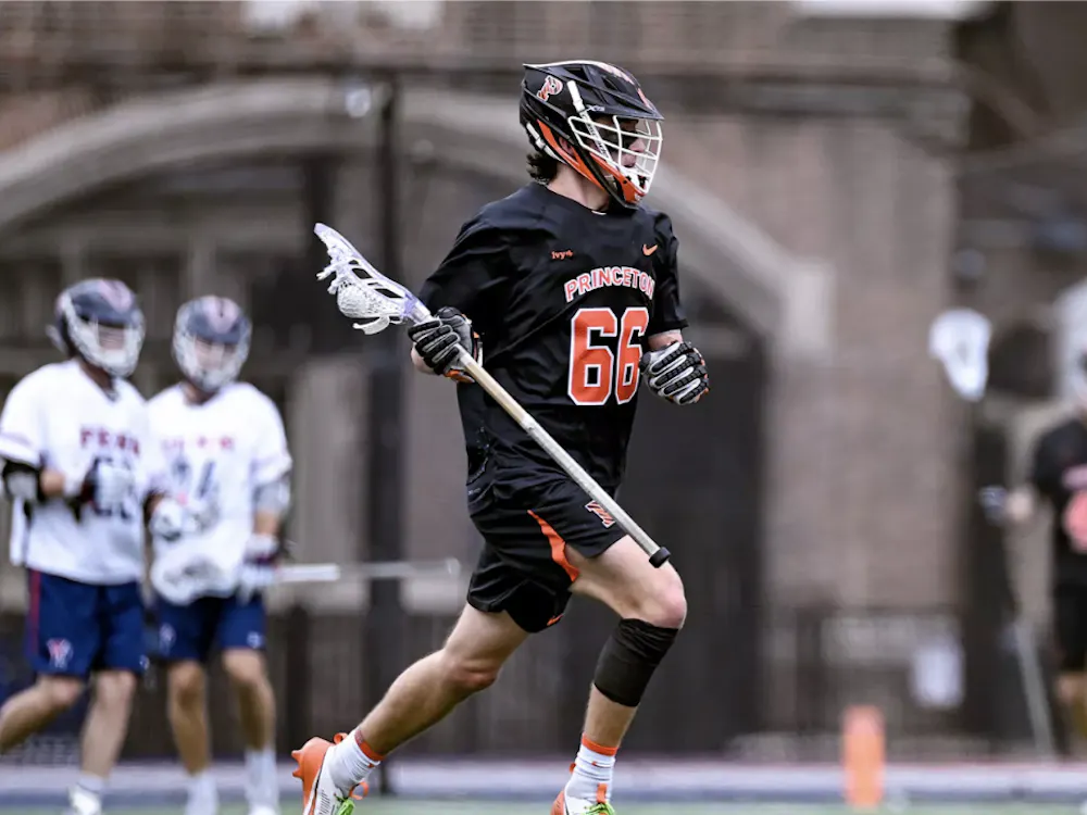 Men's lacrosse player in black uniform and orange writing holding stick behind him looking for a pass.